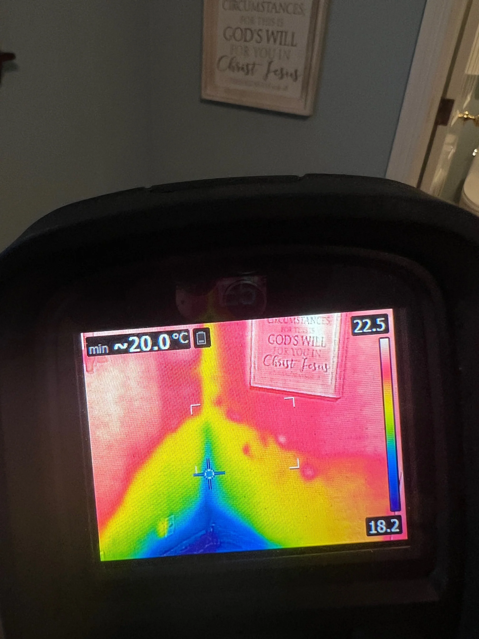 Thermal imaging camera showing varying temperatures of a wall, with a sign that reads 'Circumstances for these is Gods Will for You in Christ Jesus' in the background.