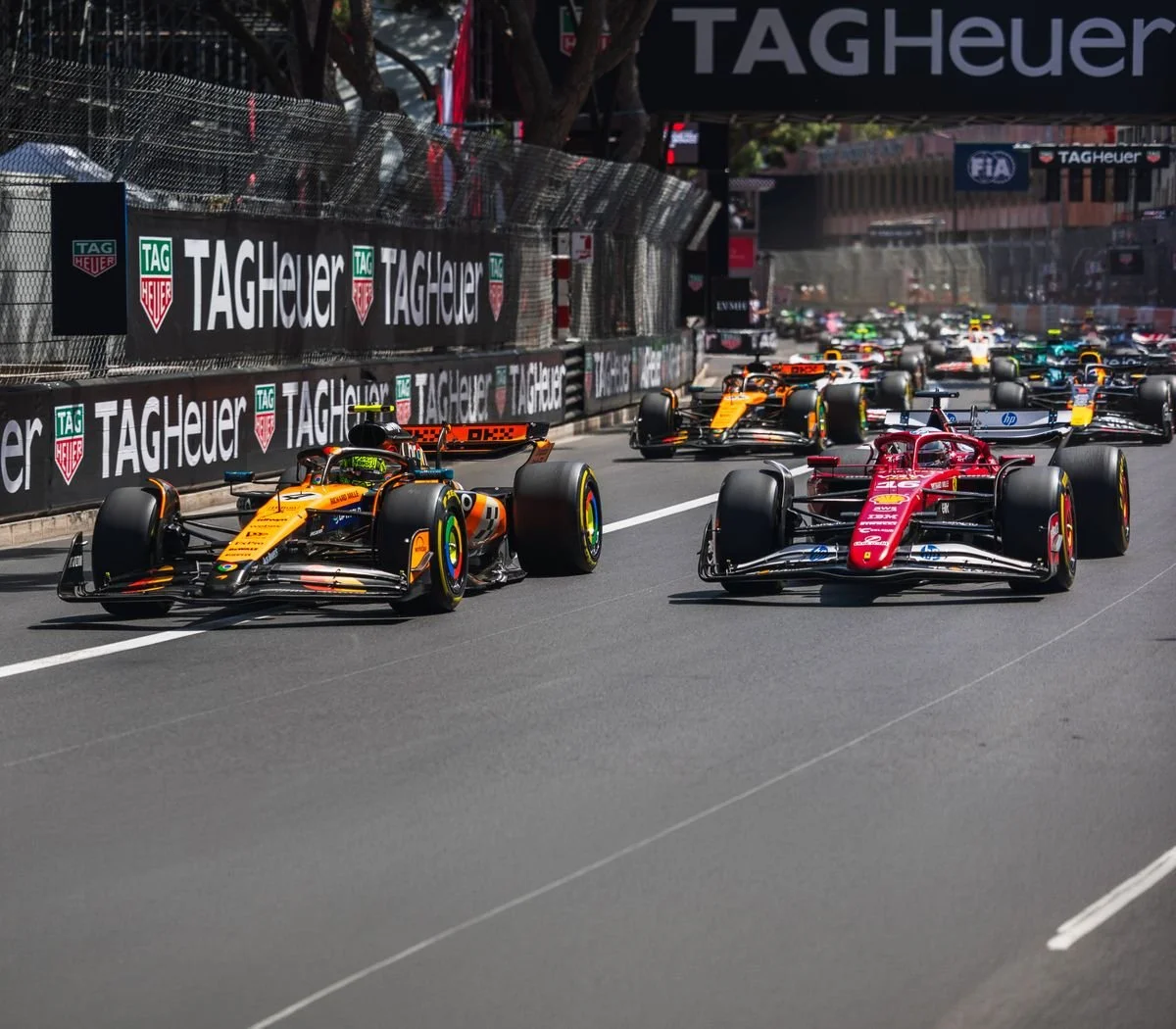 Formula 1 race cars on a city street circuit, with large TAG Heuer advertisements along the barriers.