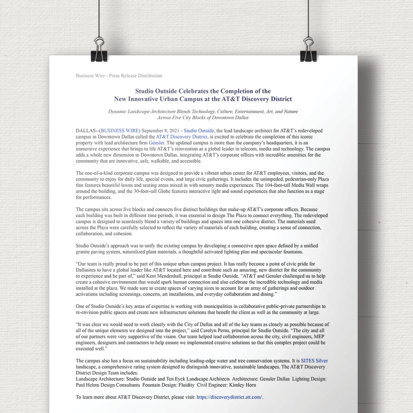 A printed press release document about the completion of the new urban campus for AT&T in Dallas, displayed on a wall with black clips.