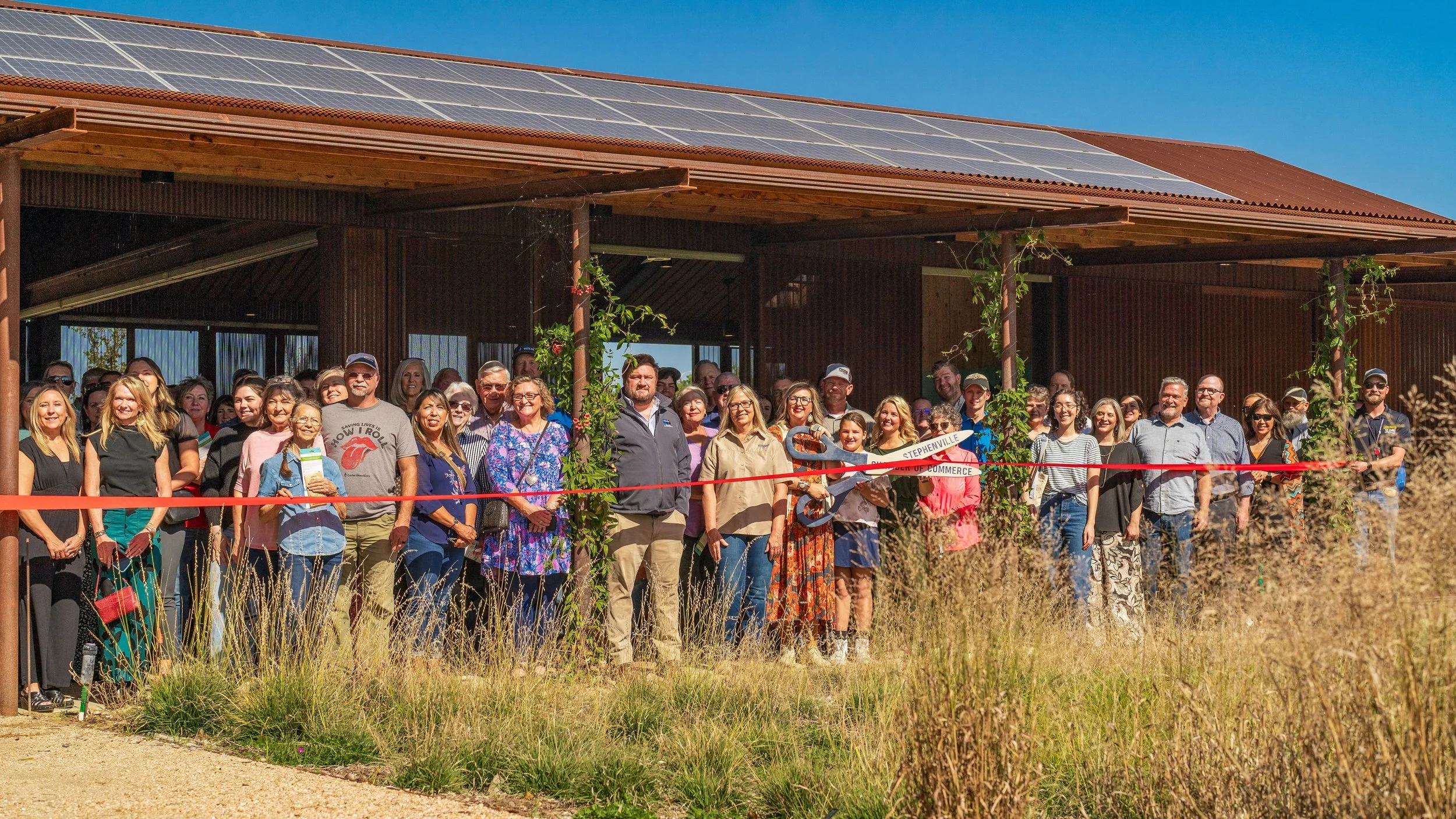 Group of people gathered for a ribbon-cutting ceremony outside a wooden building with solar panels on the roof.