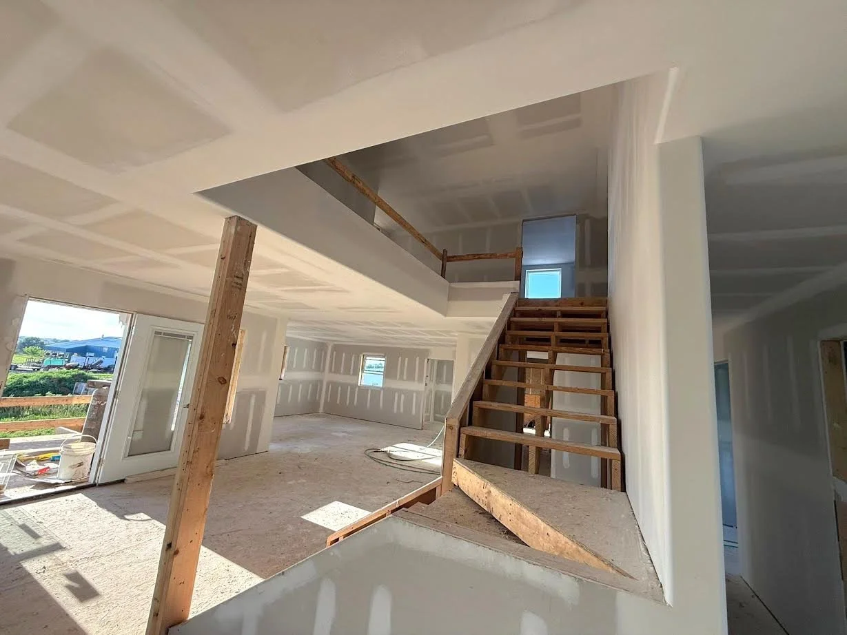 Interior of a house under construction with unfinished walls, staircase, and construction materials.