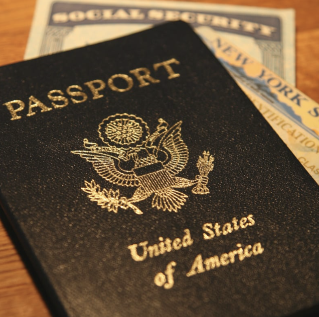A United States passport with a gold eagle emblem on the cover, placed on top of a social security card and a New York State identification card.
