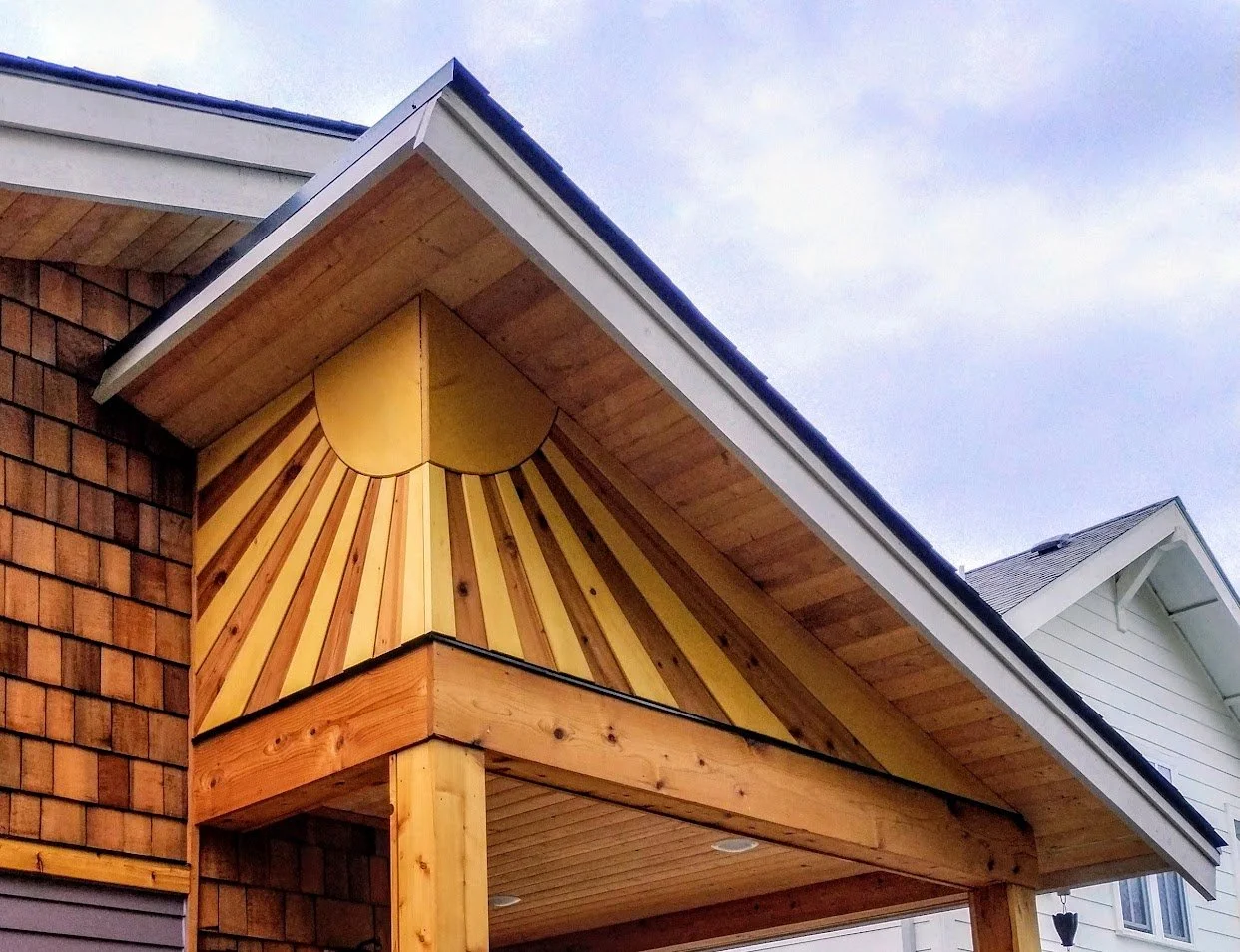 Close-up of the front porch of a house with a gable sunburst made from western red cedar and alaskan yellow cedar. Exterior wooden art piece.