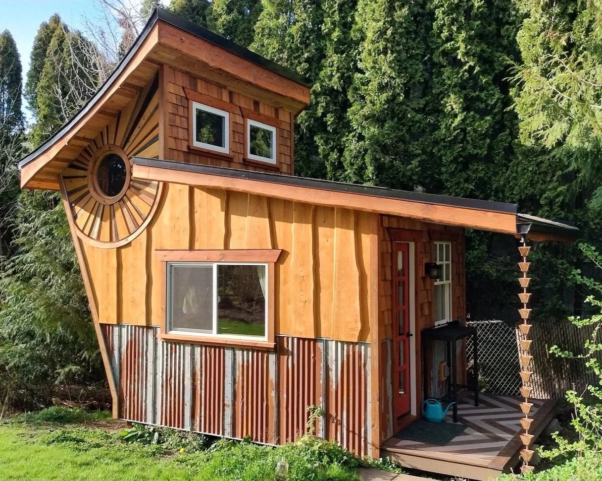 Small backyard studio with a unique creative design. A curved roof, angled wall, small covered porch, lend to its quirky personality.  It features reclaimed materials, a copper rain chain and a decorative round window with sunburst design.