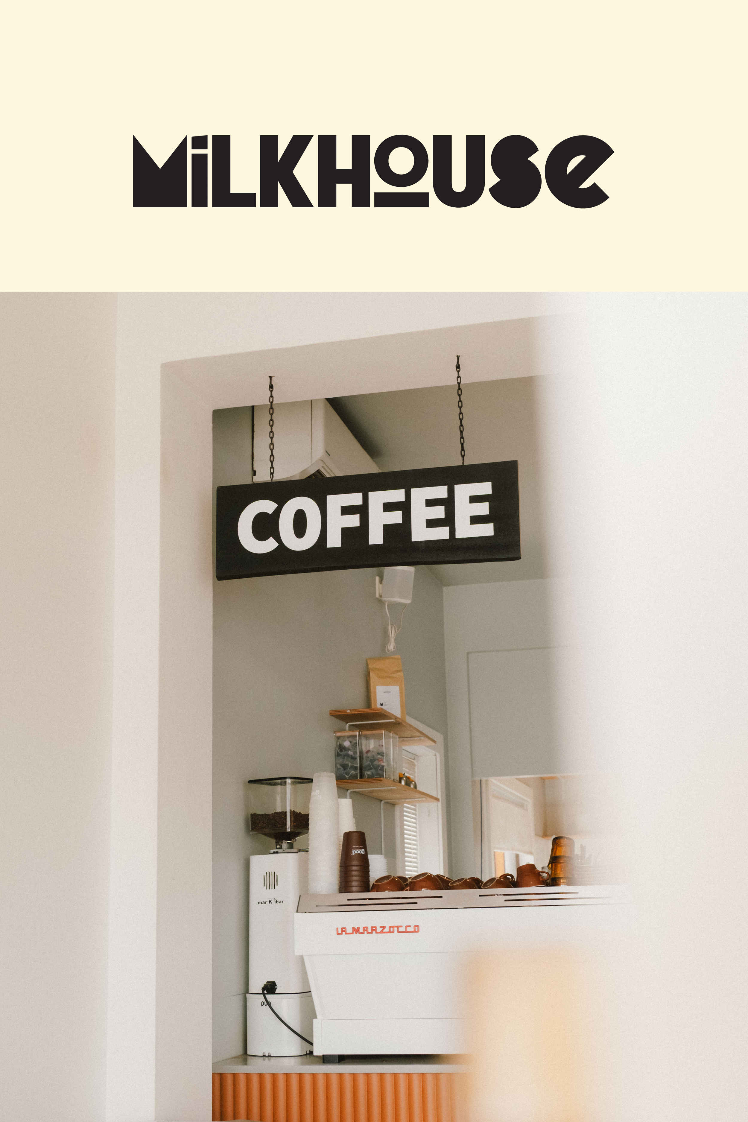 Interior of a coffee shop with a black sign hanging that reads 'COFFEE' and a larger sign above that says 'MILKHOUSE' in bold black letters.