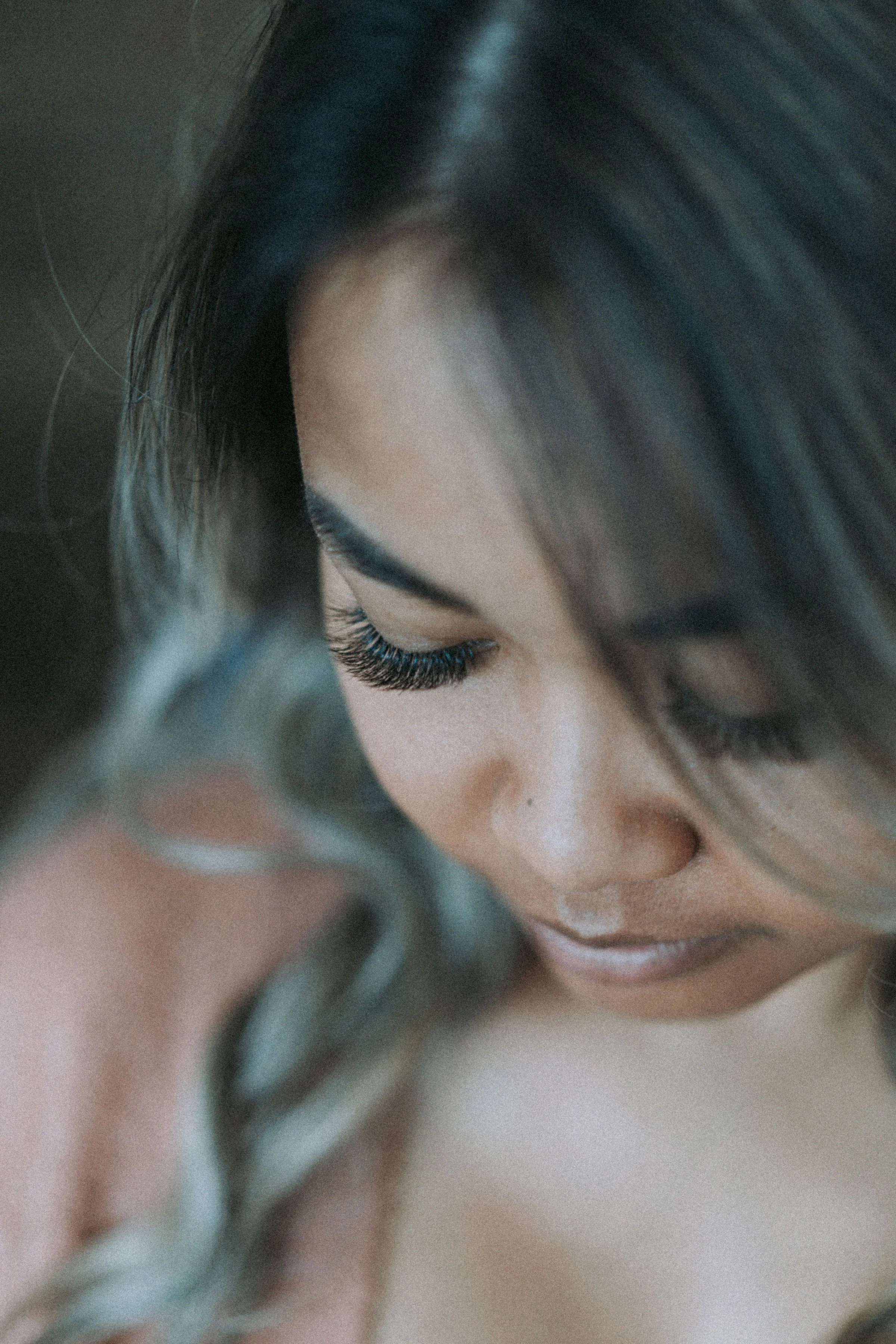 A close-up of a woman's face with her eyes closed, showing long eyelashes and dark hair.