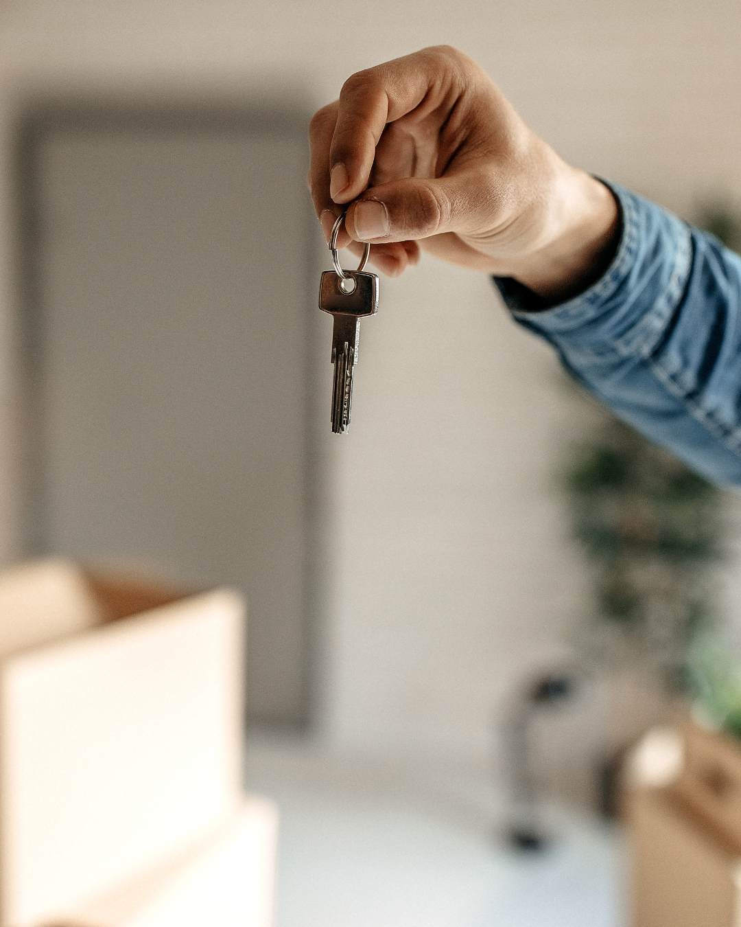 A person wearing a blue long sleeve shirt holding a key with a silver metal keyring.