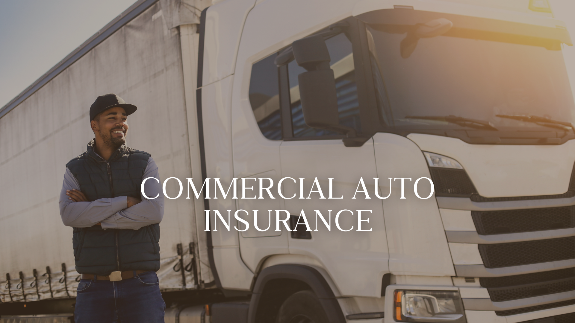 A smiling man in casual clothing standing with arms crossed in front of a large white commercial truck. The scene is outdoors with sunlight, and the truck is parked beside a concrete wall. The text overlay reads 'Commercial Auto Insurance'.