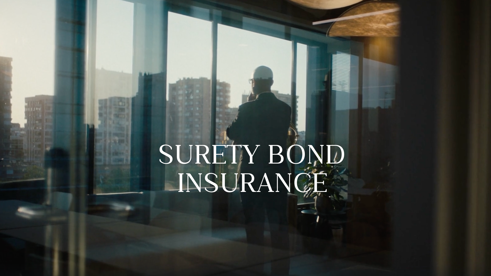 A man in a suit and glasses standing inside an office, looking out at city buildings through large windows during daylight, with the text 'Surety Bond Insurance' overlaid.