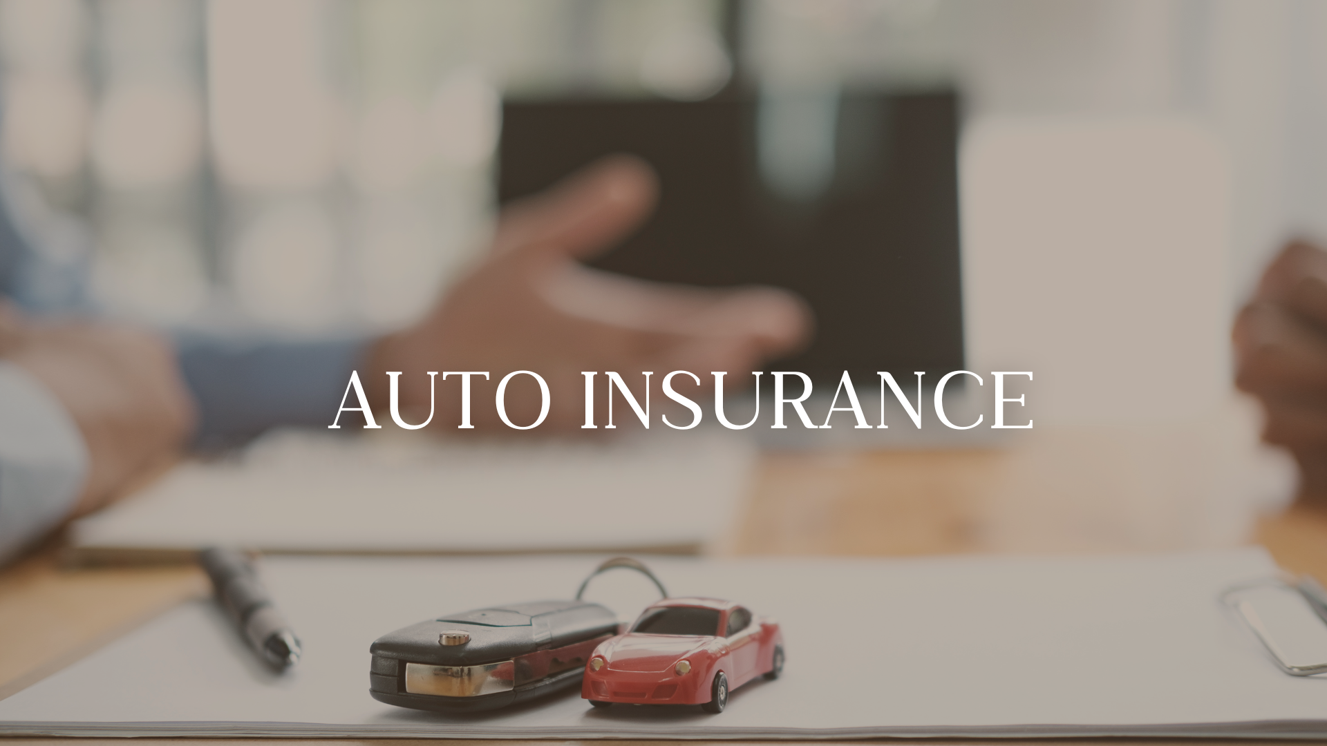 Close-up of car keys and a toy red sports car on a notepad with a pen nearby, and a person's hands holding a tablet in the background, with the text 'AUTO INSURANCE' overlayed.