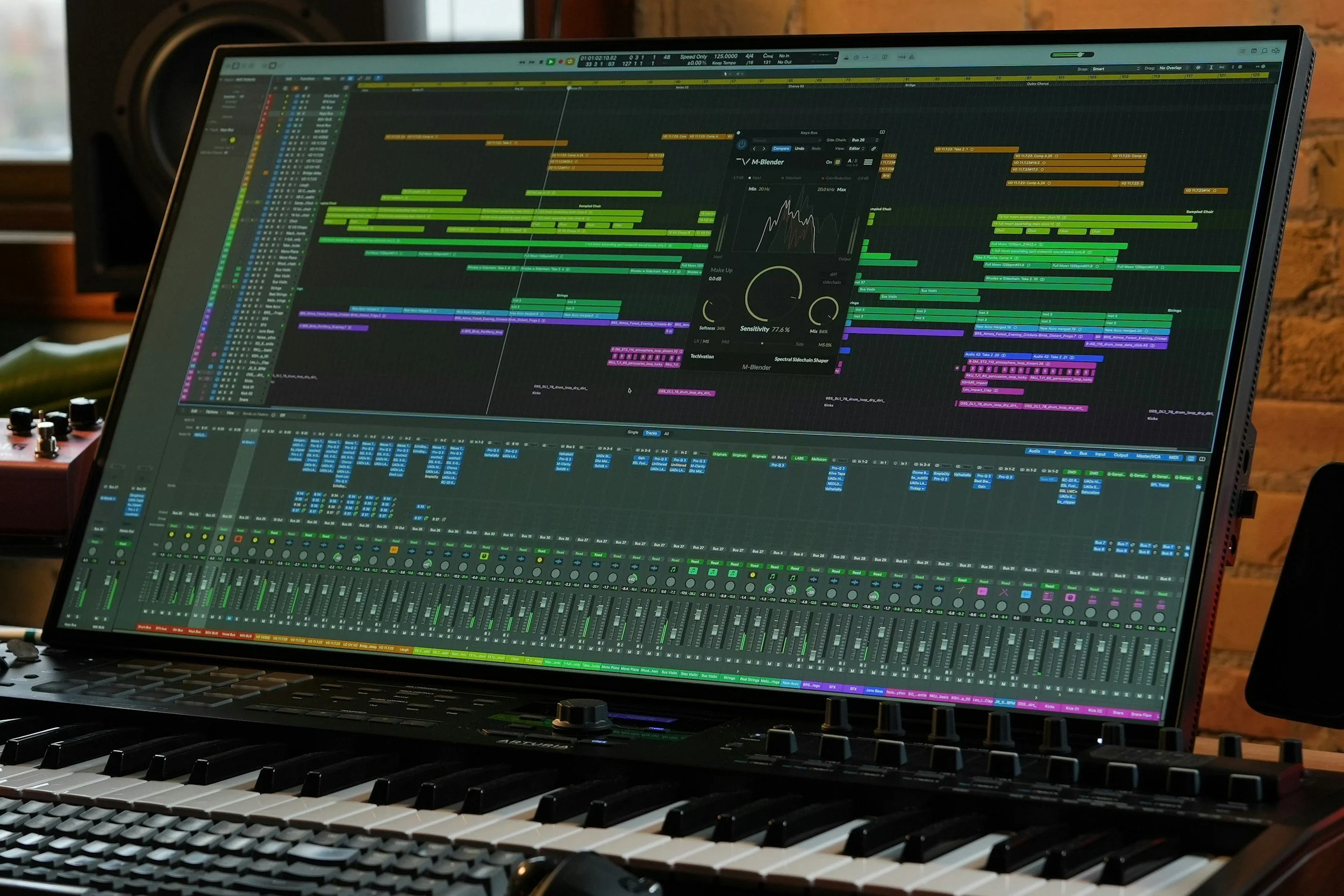 A music production setup with a computer monitor displaying digital audio workstation software, a MIDI keyboard, and a MIDI controller, all placed on a desk in a room with wooden walls.