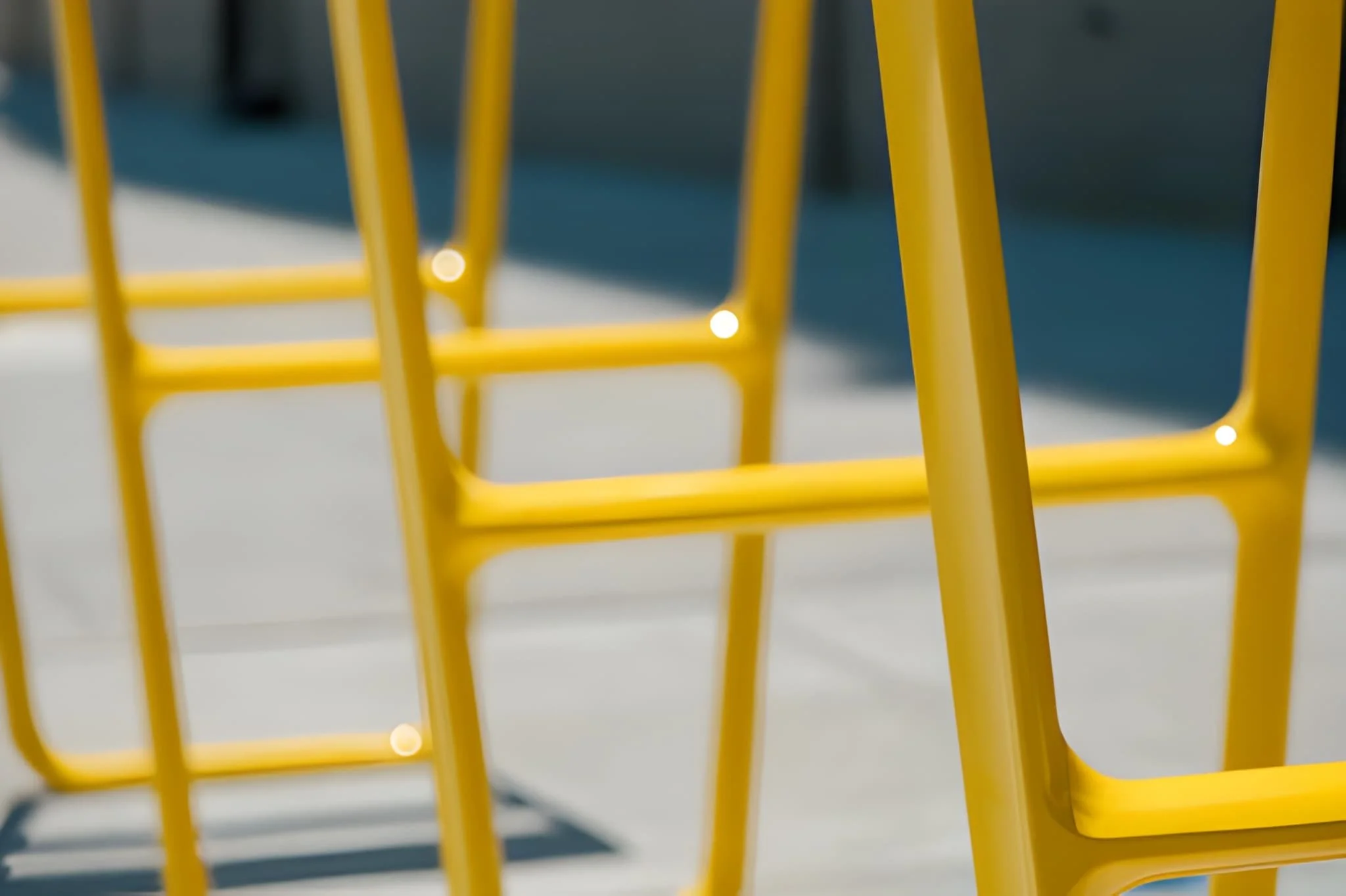 Close-up of yellow metal chair frames on a white surface with shadows.