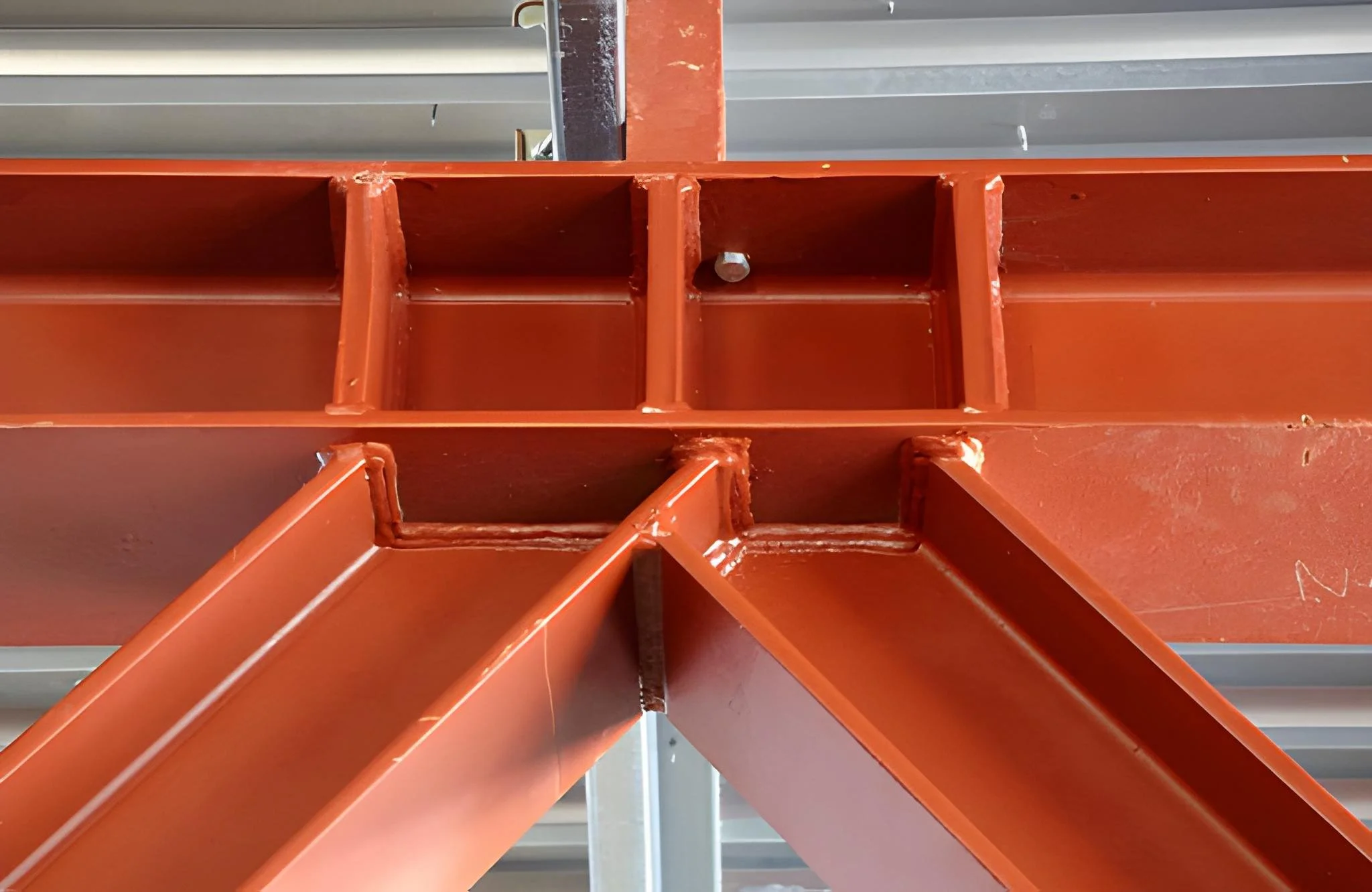 Close-up view of a large orange steel support beam with reinforcing plates and fasteners, part of a building's structure.