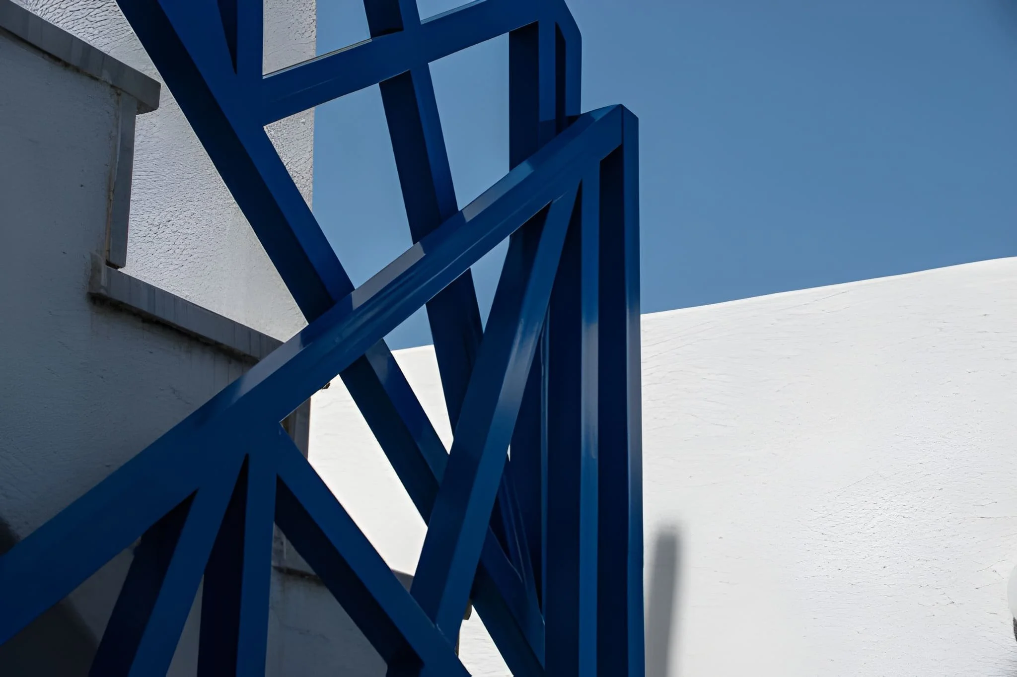 Close-up of a blue metal railing attached to a white wall with a clear blue sky in the background.