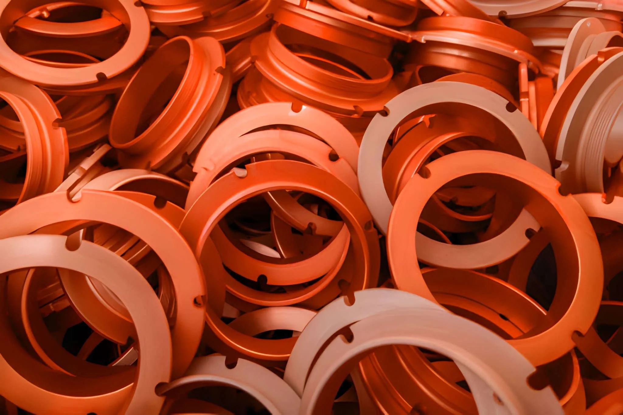 A pile of orange plastic rings with notches and small holes.