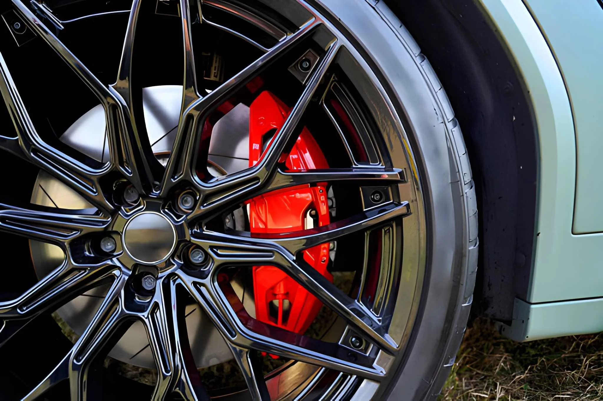 Close-up of a car wheel featuring a black alloy rim with a complex spoke design, a prominent red brake caliper behind the rim, and a tire mounted on the wheel.