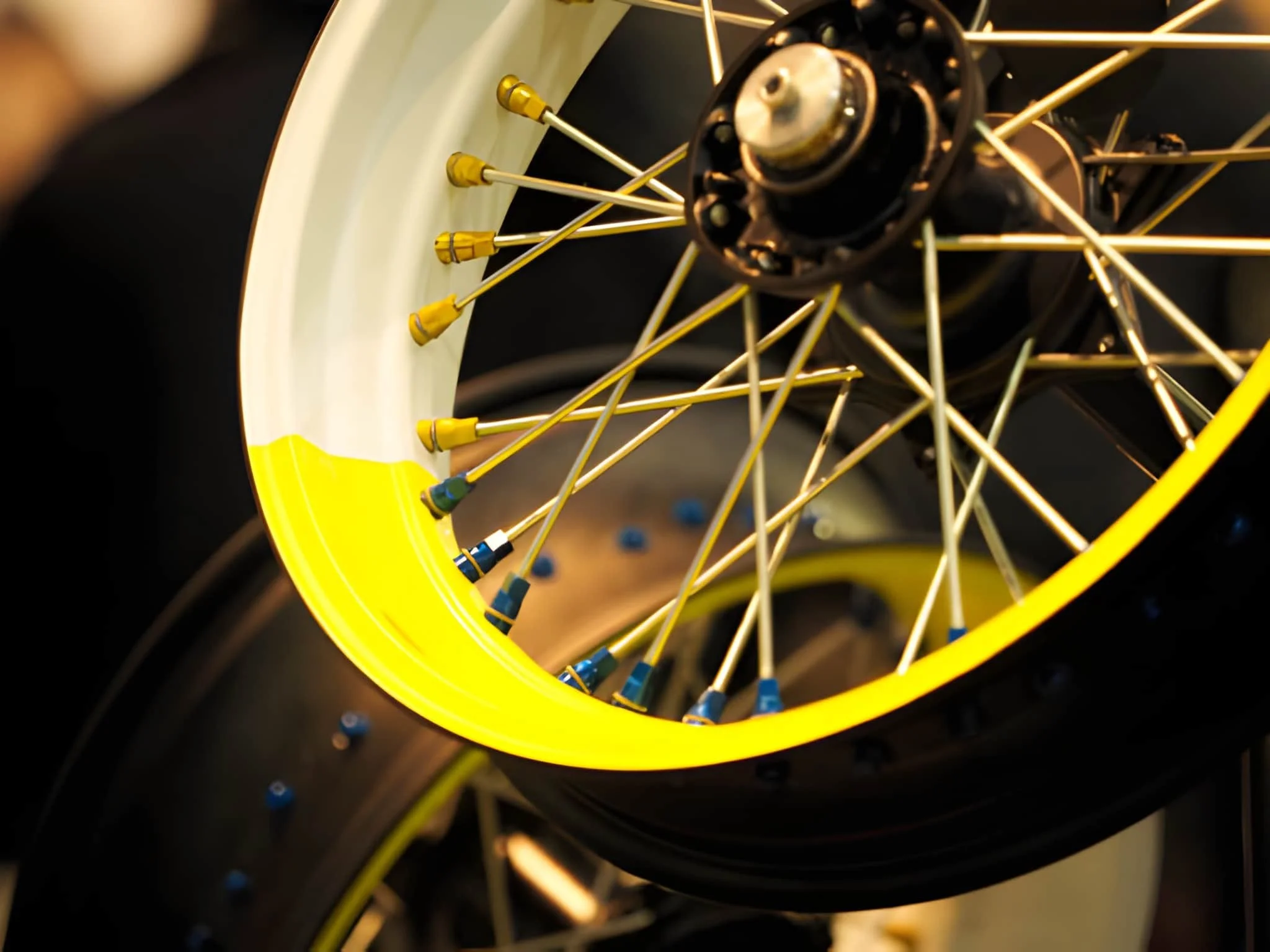 Close-up of a racing bicycle wheel with yellow hub, yellow spokes, and yellow rim, showing part of the tire and valve holes.