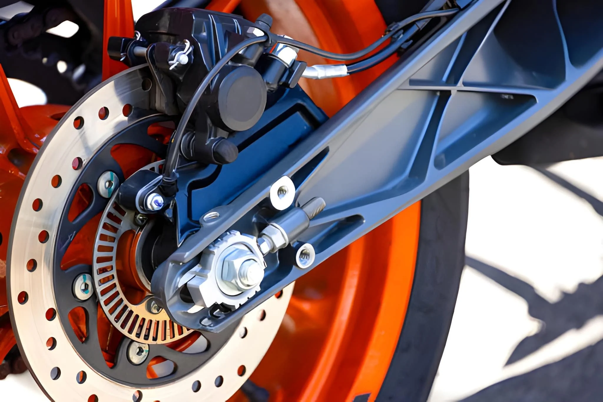 Close-up of a motorcycle's front disc brake system with a black caliper, silver brake rotor, and orange wheel rim.