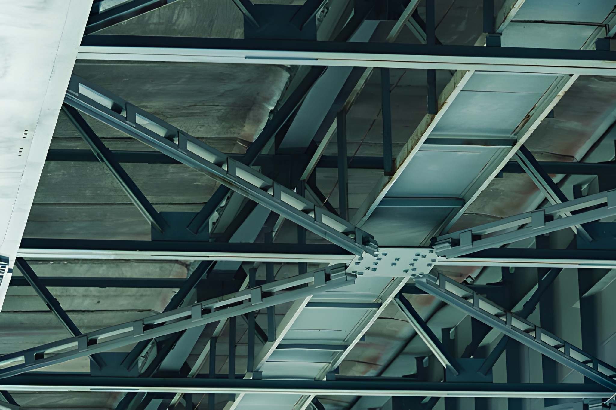 A view looking up at a modern building's exposed structural framework, showing metal beams, escalators, and glass windows from below.