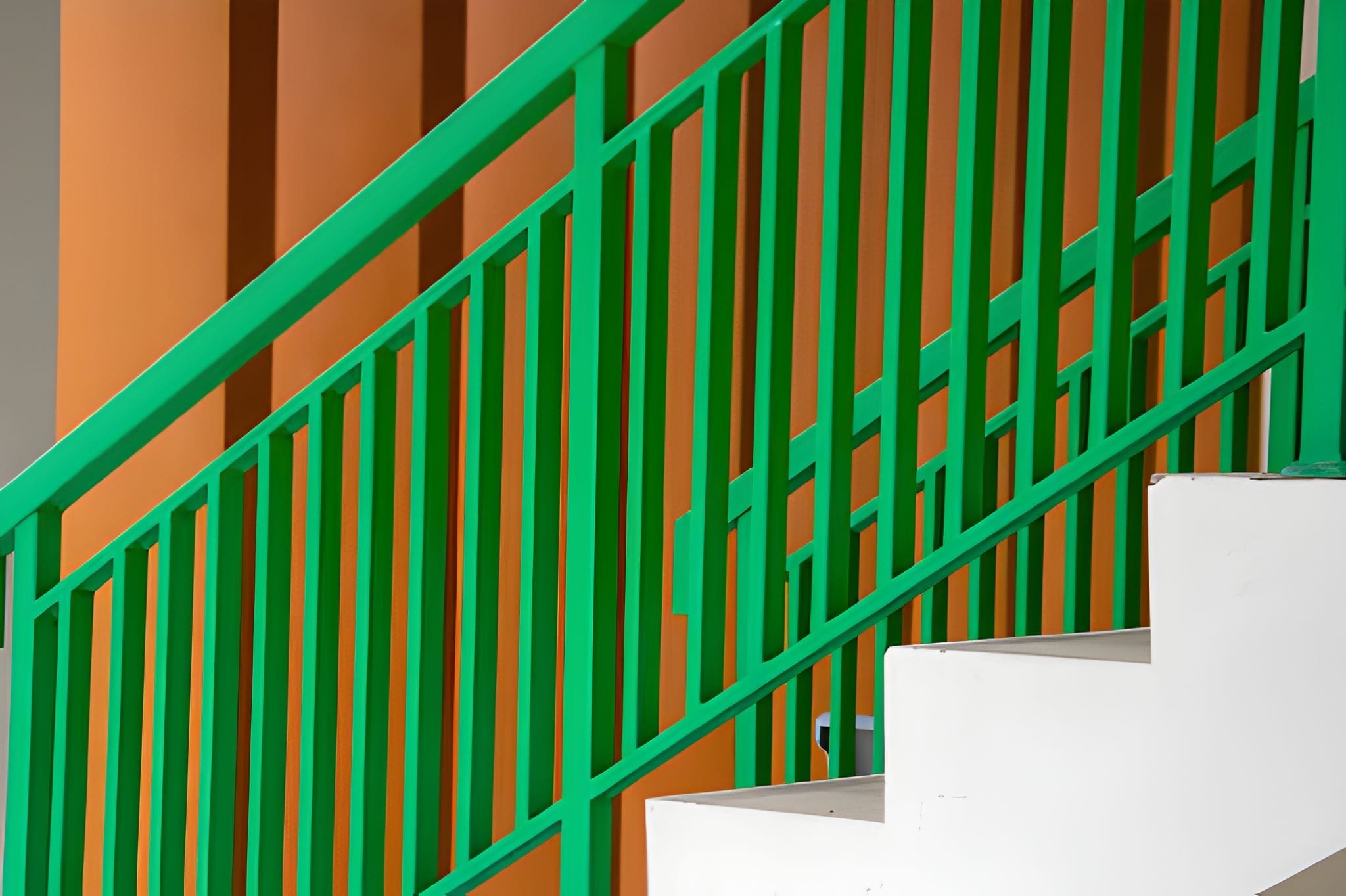 A staircase with white steps and a green railing against a brown wall.