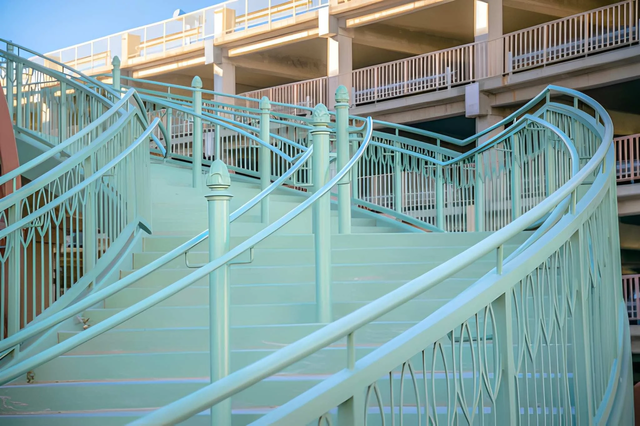 Empty pastel blue outdoor staircase with curved handrails leading up to a multi-level parking garage.