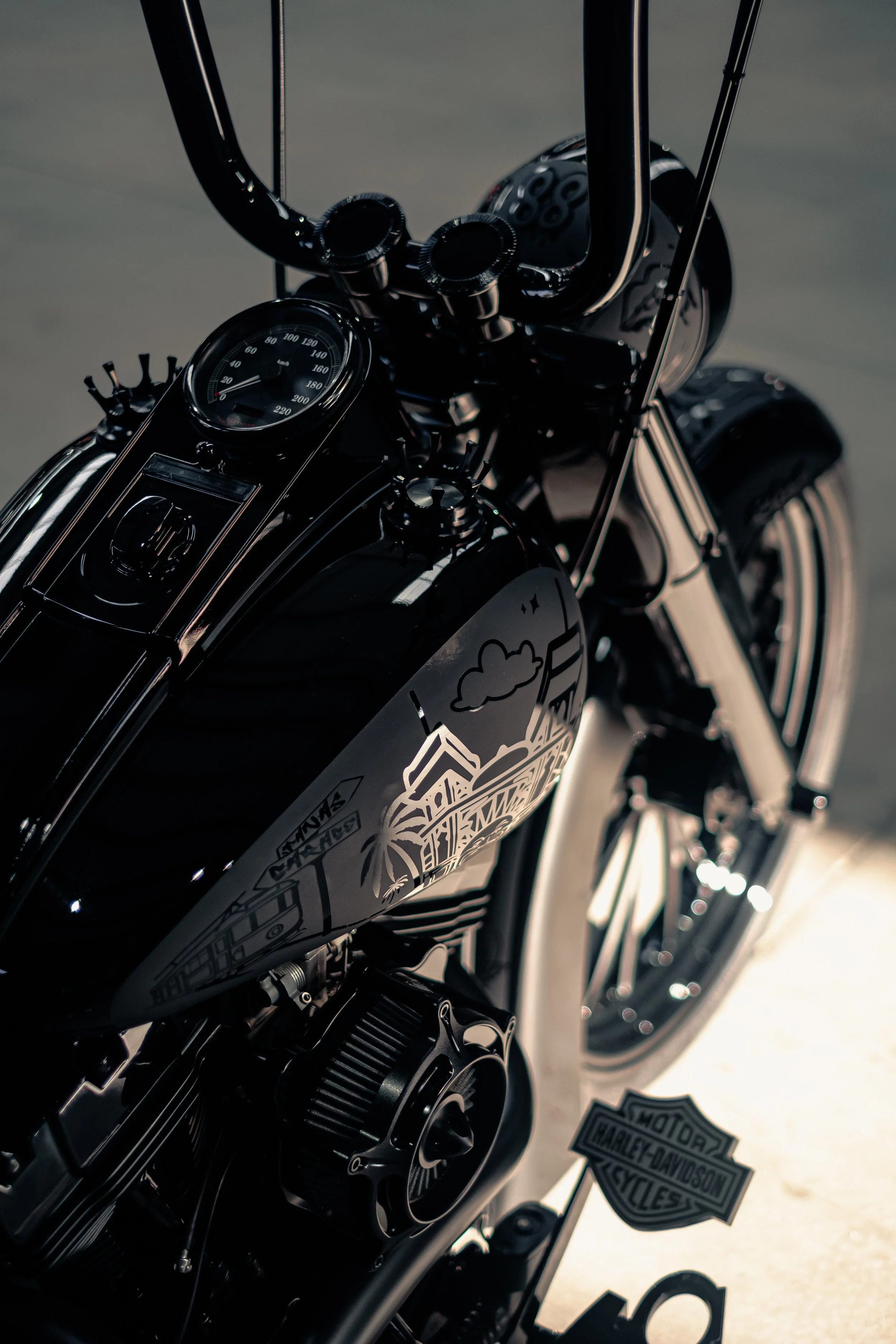 Close-up of a black Harley-Davidson motorcycle, showing the fuel tank with a graphic design, the speedometer, and parts of the handlebars and front wheel.