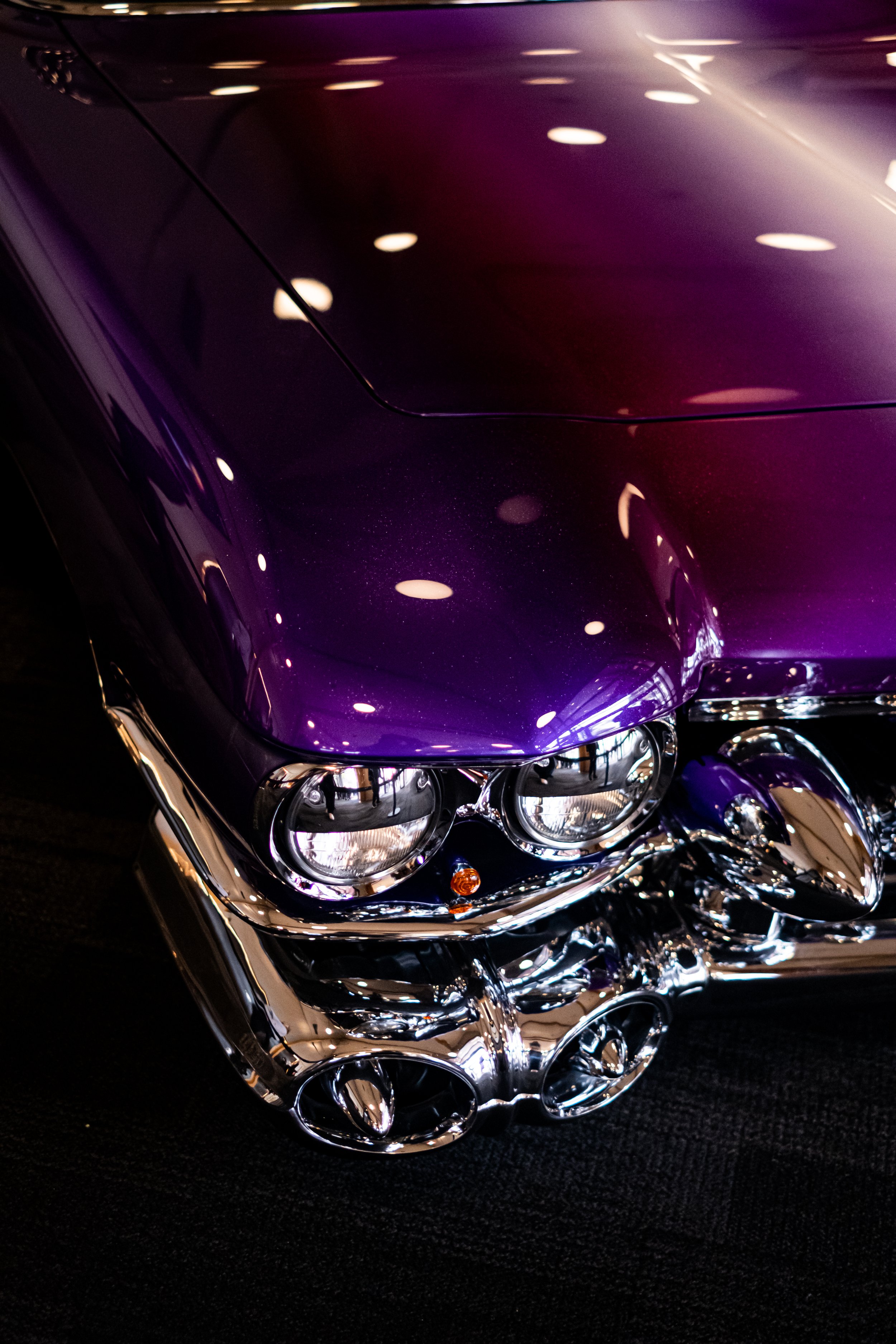 Close-up of the front of a purple and chrome vintage car, showcasing the headlights and shiny chrome details.