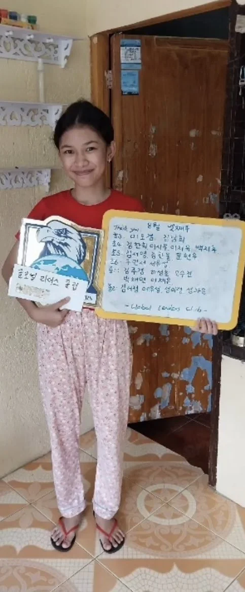 A young girl holding a whiteboard and a sports award in a room with tiled floors and a wooden door.