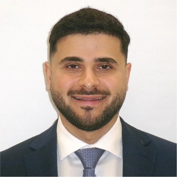Portrait of a man in a business suit with a white shirt and blue tie, smiling against a plain white background.