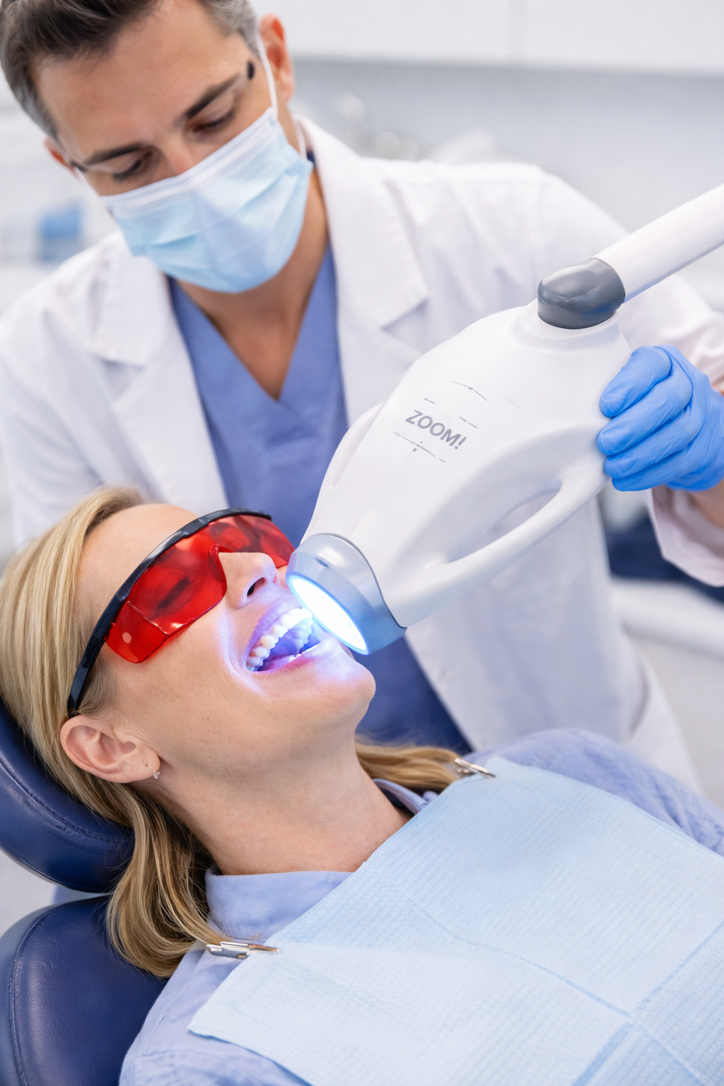 Dentist using a dental curing light on a patient wearing red protective glasses in a dental office.