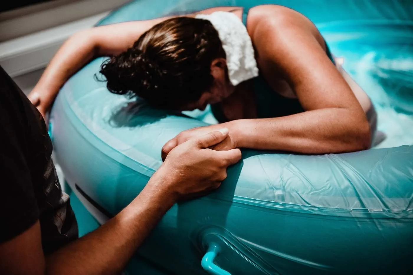 A woman in a white dress is lying on an inflatable pool float, holding onto the edge, with a person helping her.