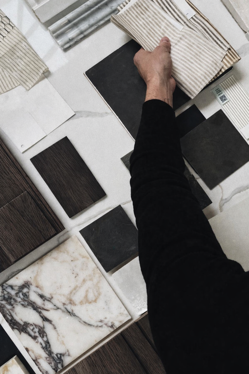 A hand flipping through a book of tile samples with various tile designs and colors, including marble, wood, and stone textures, on a display table.