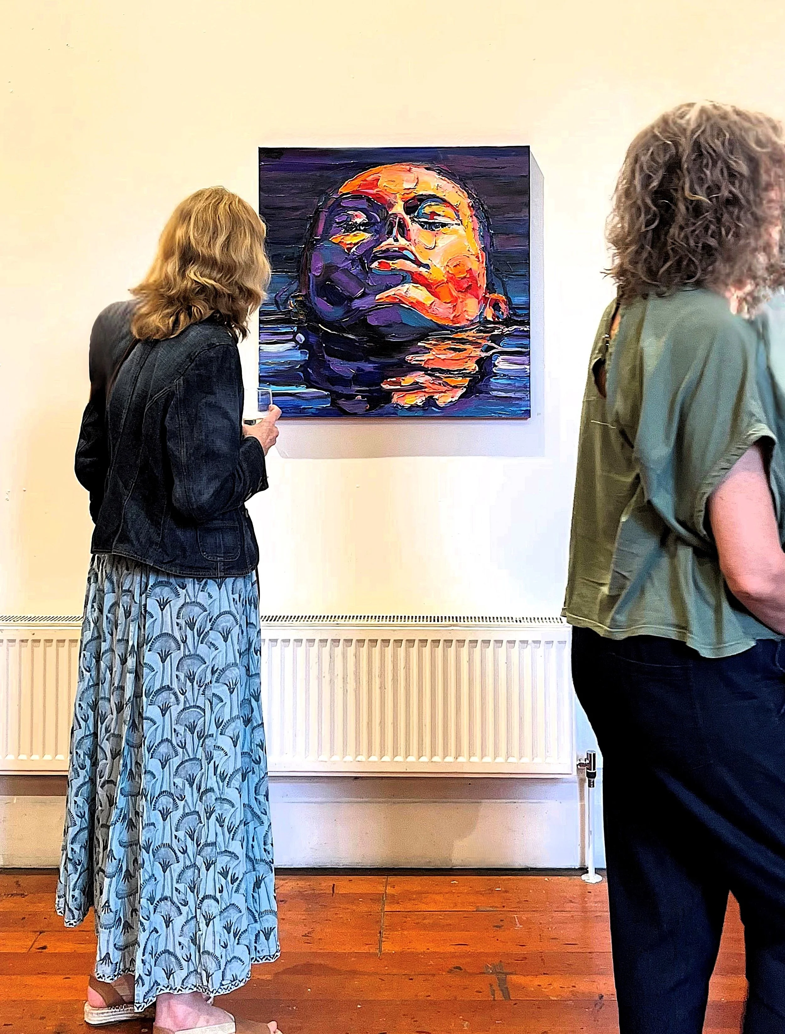People viewing a colourful painting by Simon Olsen of a women's face reflected in water at an art gallery.