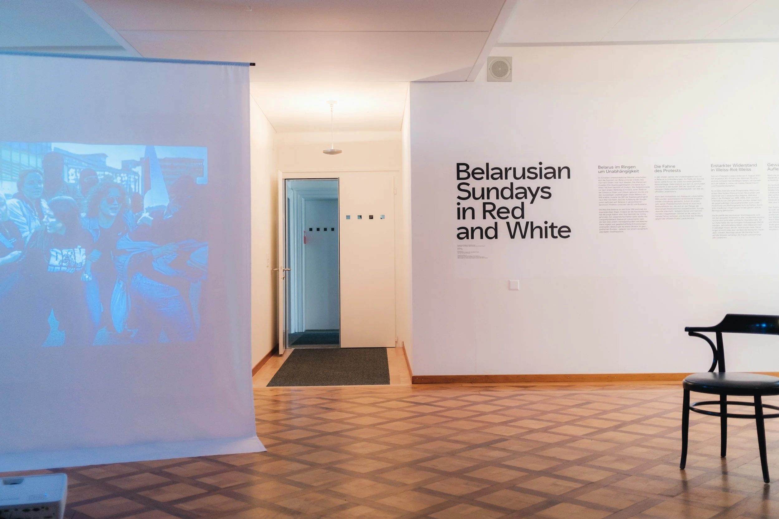 Memorial exhibit with a projection of a group of people, and a white wall with text panels.