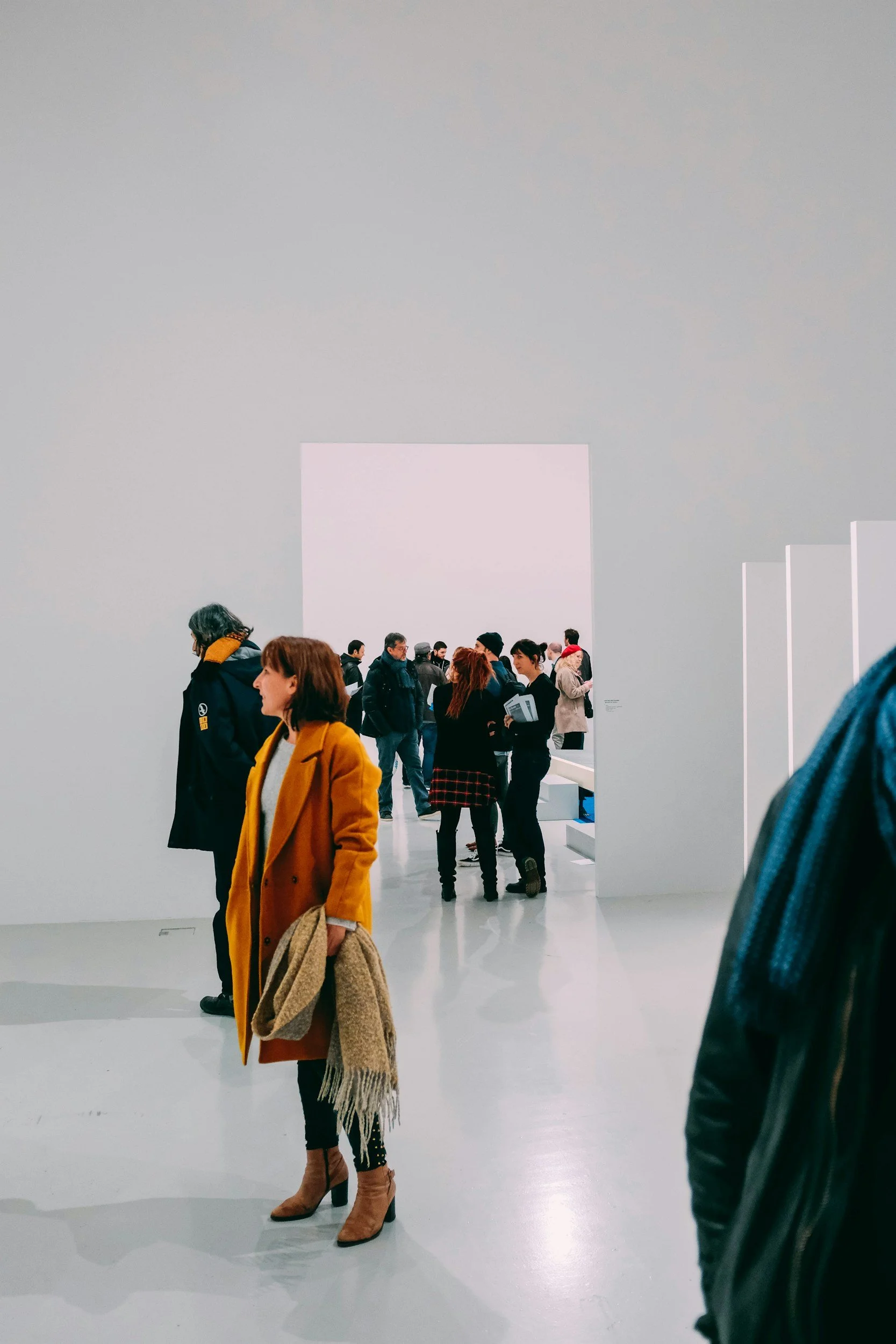People viewing photographs in a modern art gallery with white walls and polished floor, some looking at pieces and others engaged in conversation.