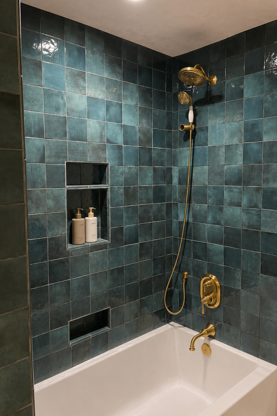 Bathroom shower with green tiles, gold fixtures, a showerhead, and bottles of soap in a niche.
