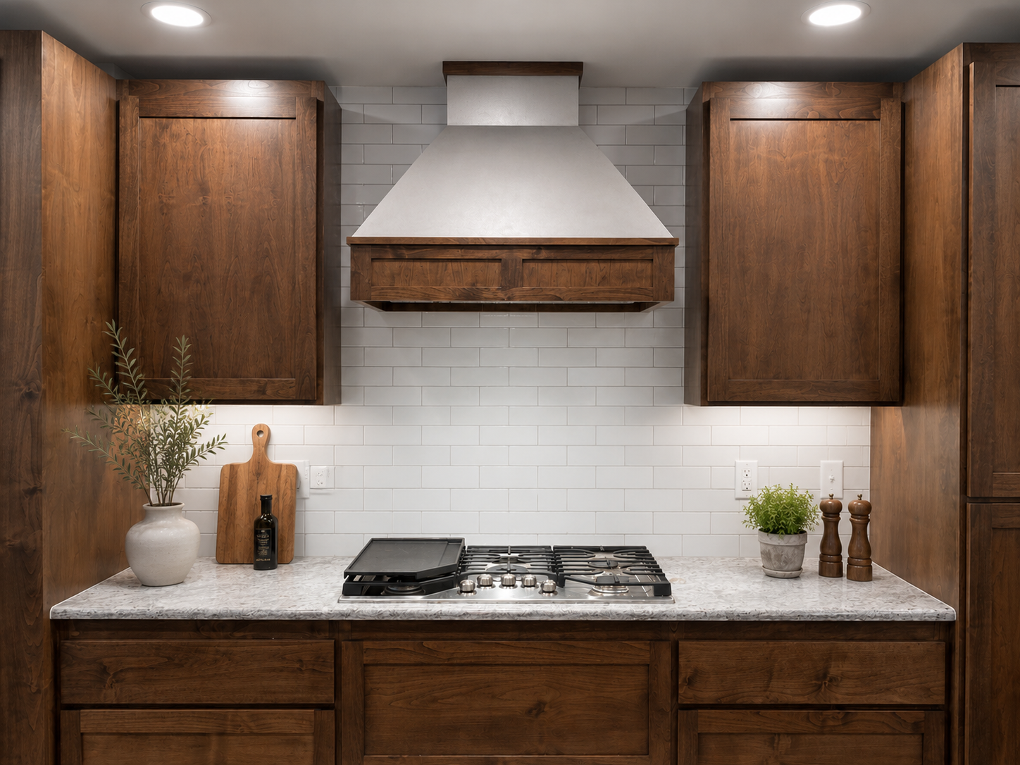 Kitchen with white subway tile backsplash, wooden cabinets, stainless steel range hood, granite countertop, potted plants, salt and pepper shakers.