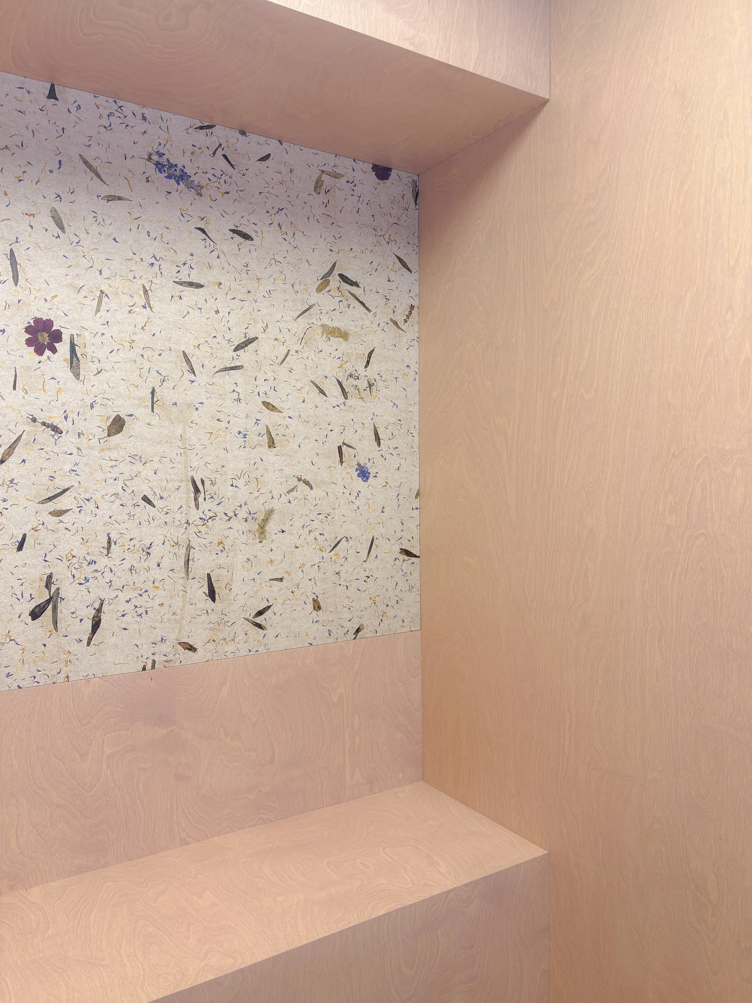 A wooden corner with a speckled granite countertop and two light pink wooden walls meeting at a right angle.