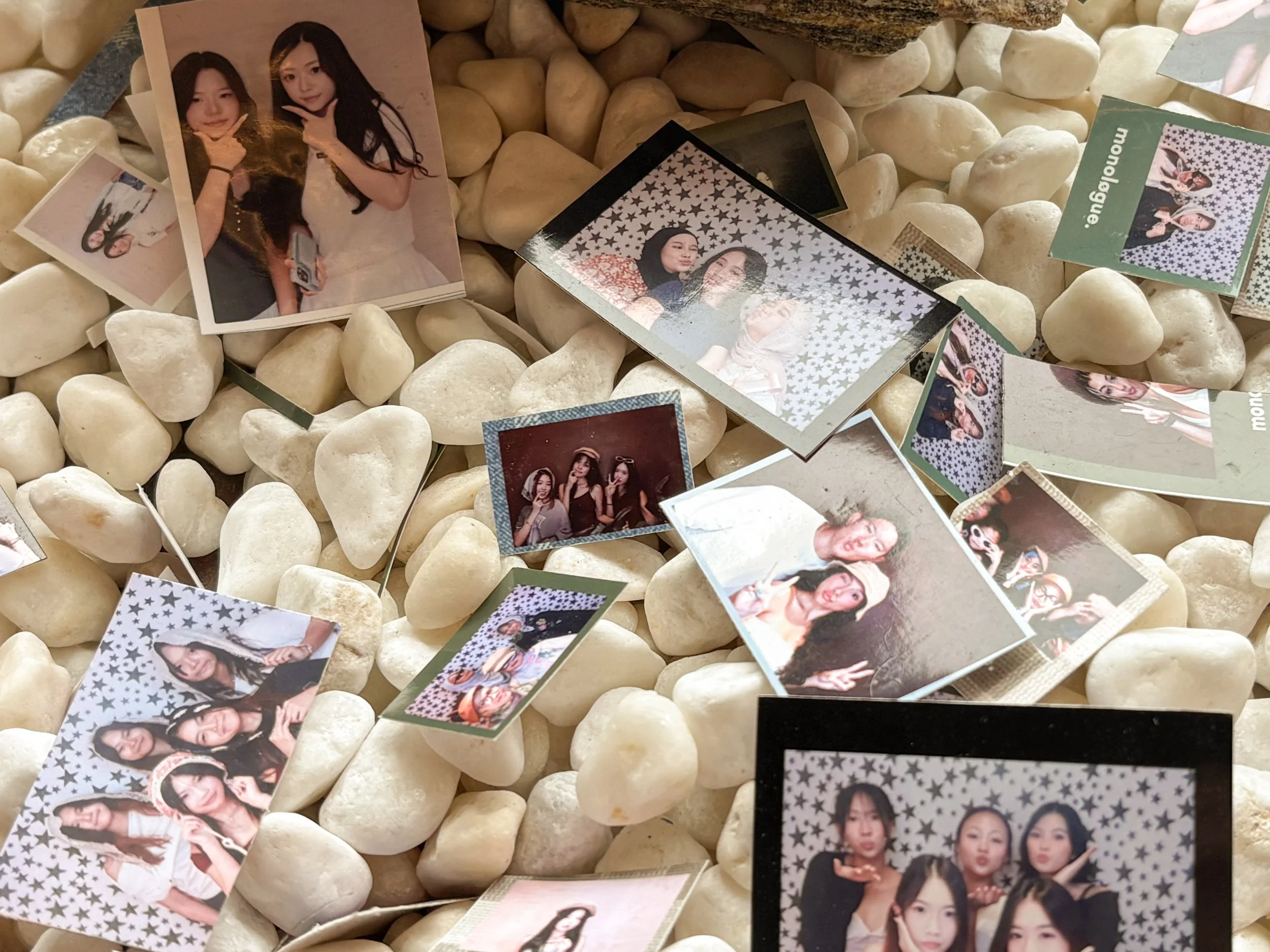 Multiple printed photos of young women on a bed of white stones, some photos are in color with star-patterned backgrounds, others are candid images of friends posing and smiling.