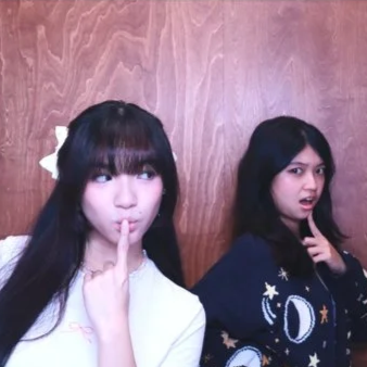 Two young women making silly faces in front of a wooden wall.
