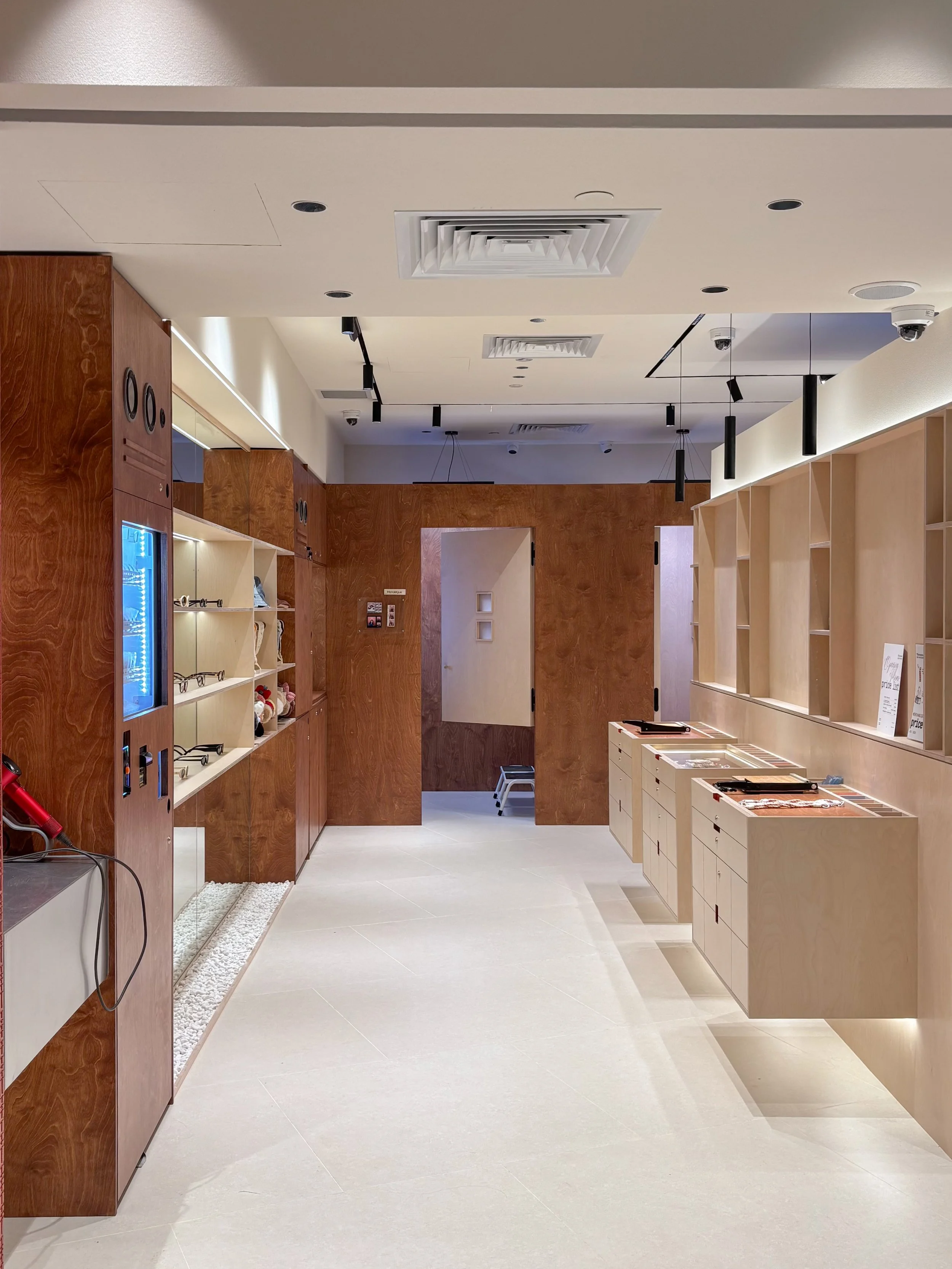 Interior view of a modern shop or gallery with wooden and light-colored display shelves, a vending machine, ceiling vents, and security cameras.