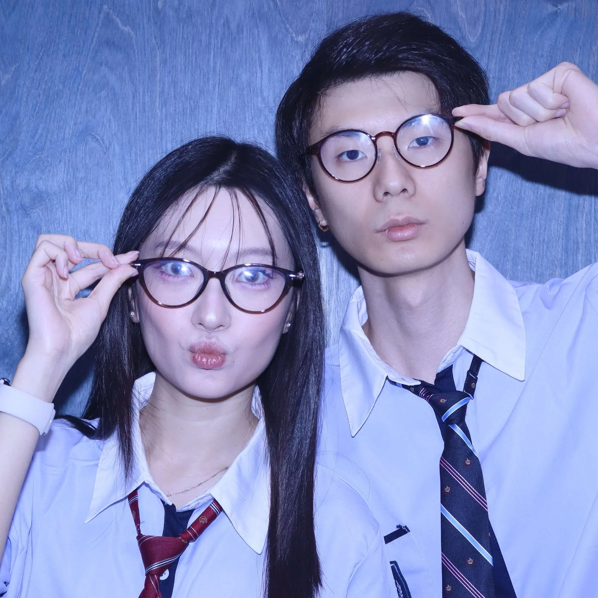 Two women wearing glasses and white shirts appear to be posing and adjusting their glasses against a blue background.
