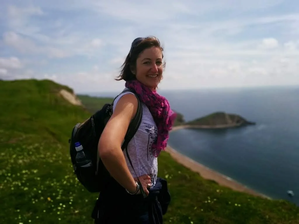 A woman hiking on a grassy coastline with cliffs and the ocean in the background.