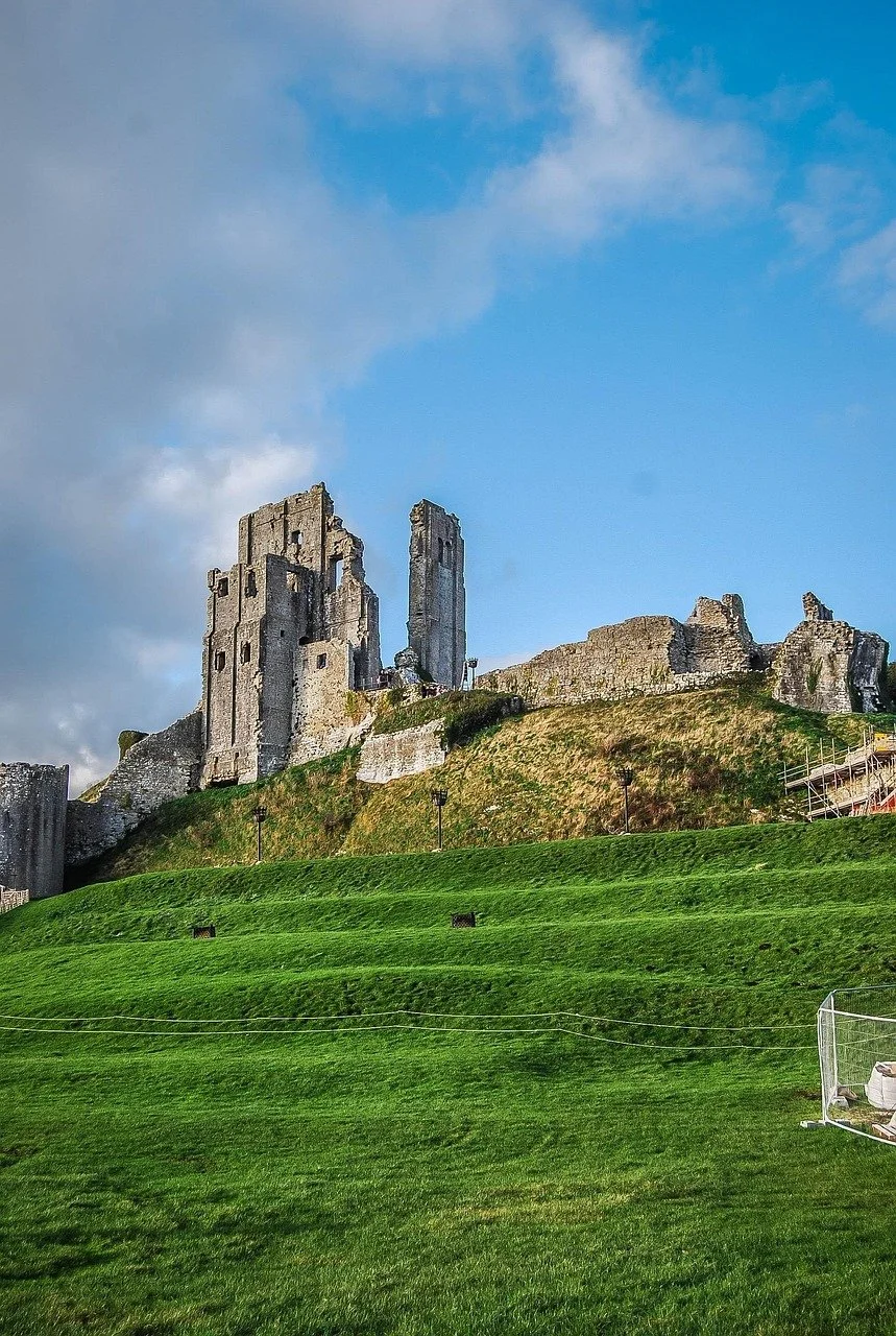 Ruins of an ancient castle on a grassy hill under a partly cloudy blue sky.