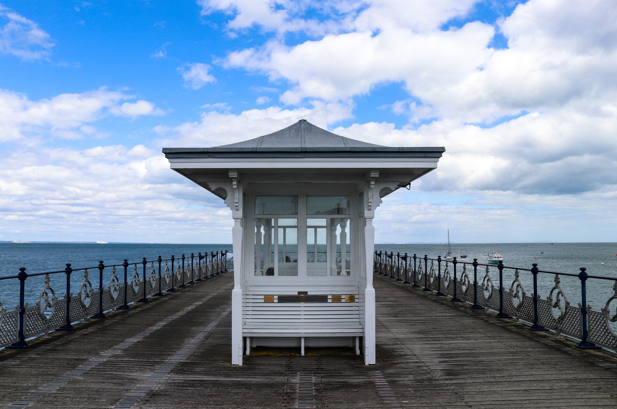 A wooden pier extending over the ocean with a small white gazebo at the center, under a partly cloudy sky.
