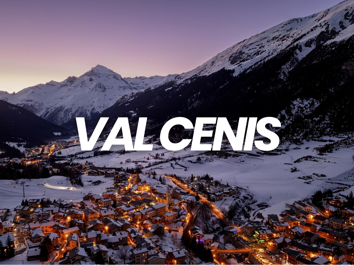 Vue d'une ville enneigée dans les Alpes avec montagnes en fond, éclairages urbains la nuit.