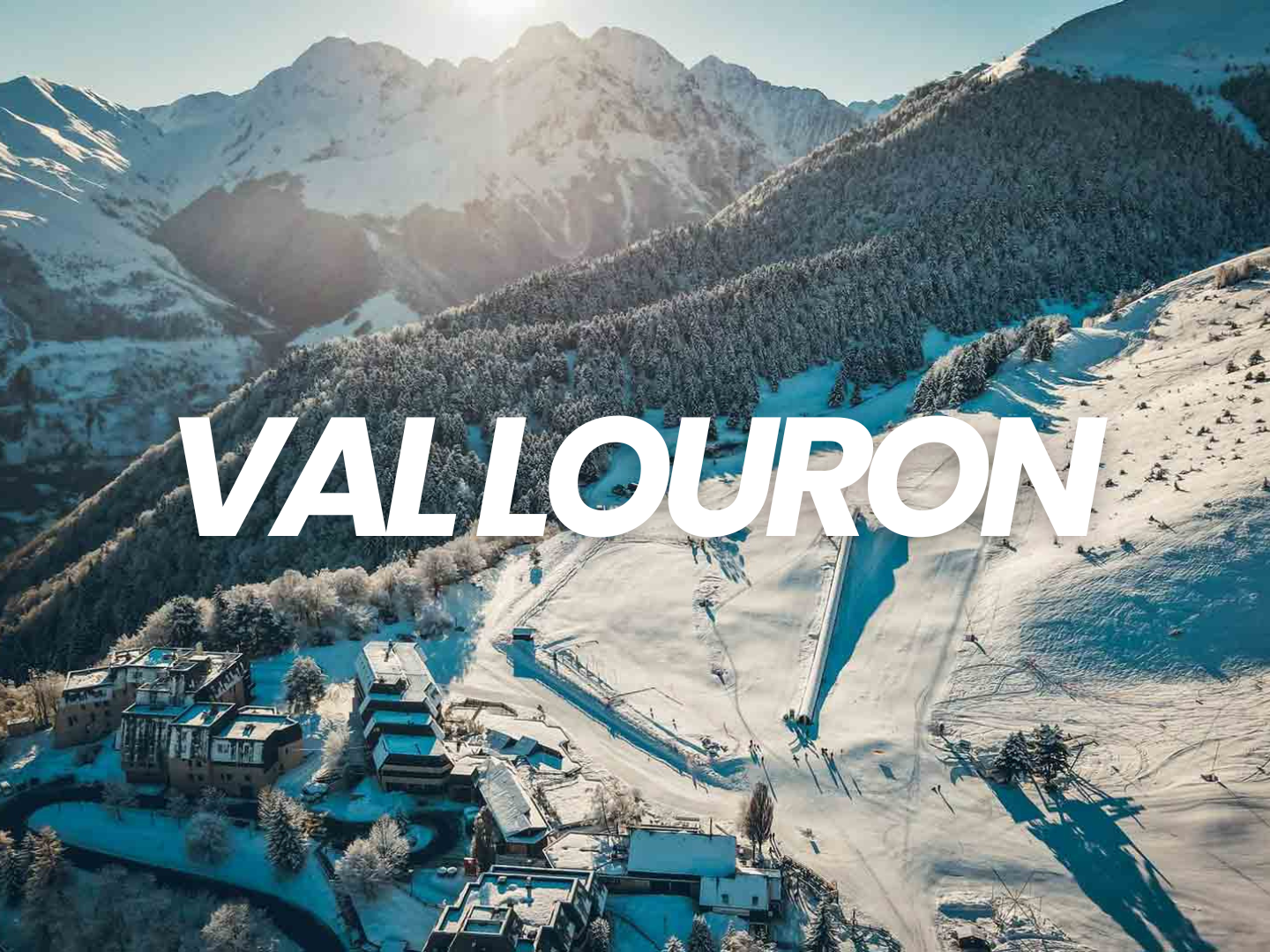 Paysage enneigé dans les montagnes avec des bâtiments, des forêts et une vallée, sous un ciel ensoleillé, avec le mot 'Vallouron' en surimpression.