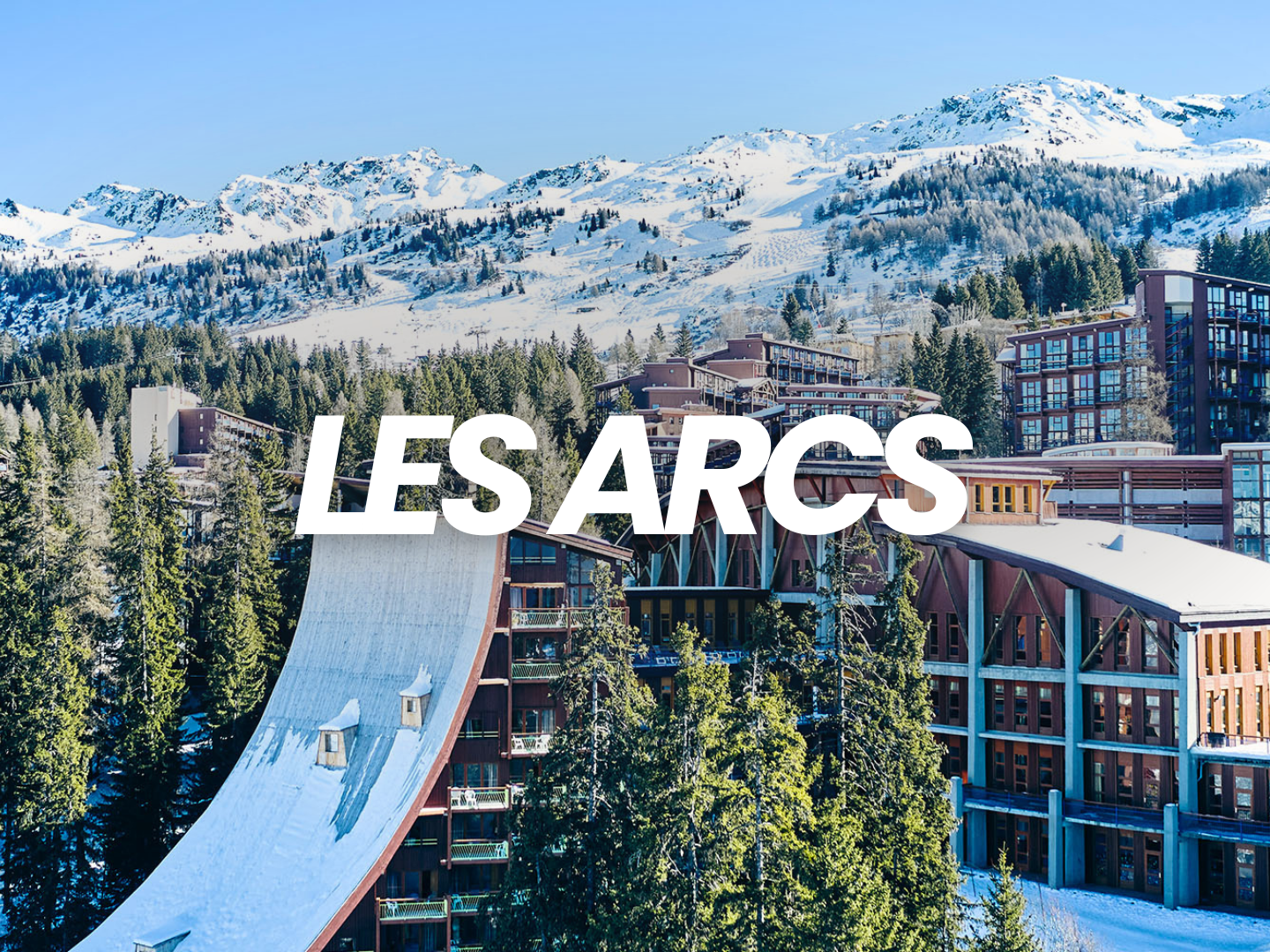 Les Arcs, station de ski avec des bâtiments modernes entourés de forêts et de montagnes enneigées sous un ciel bleu.