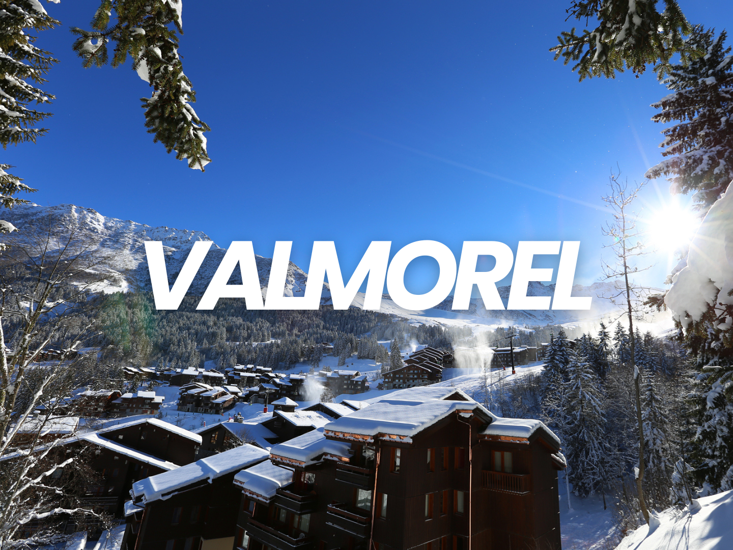 Vue d'une station de ski en hiver avec des chalets en bois recouverts de neige, des montagnes en arrière-plan, et le soleil brillant dans un ciel bleu clair.