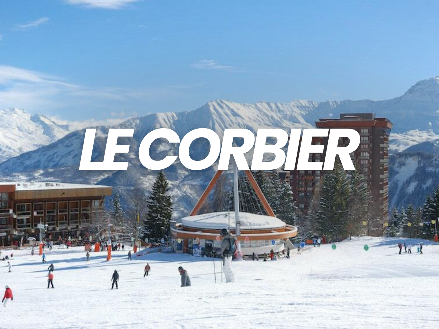 Station de ski en montagne avec des skieurs, des bâtiments et un grand disque en forme de roue, fond de montagnes enneigées et ciel bleu.